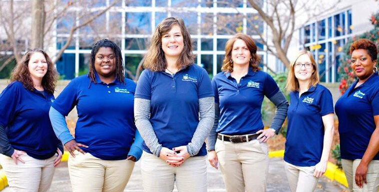 A group of women in blue shirts standing in front of a building.