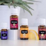Four essential oils on a table next to a plant.