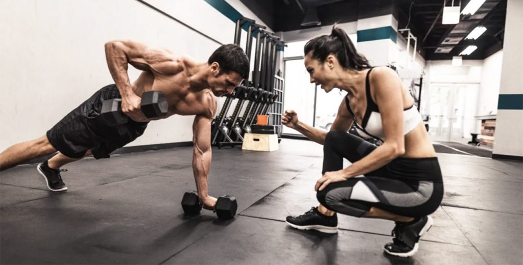 A man and woman doing push ups in a gym.