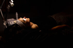 A woman laying on a bed with a light on her face.