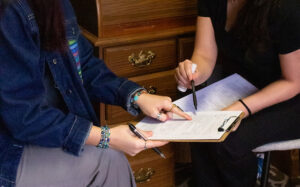 Two women sitting at a desk with a clipboard in front of them.