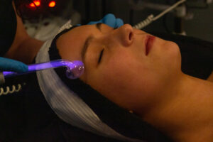 A woman getting a facial treatment with a purple light.
