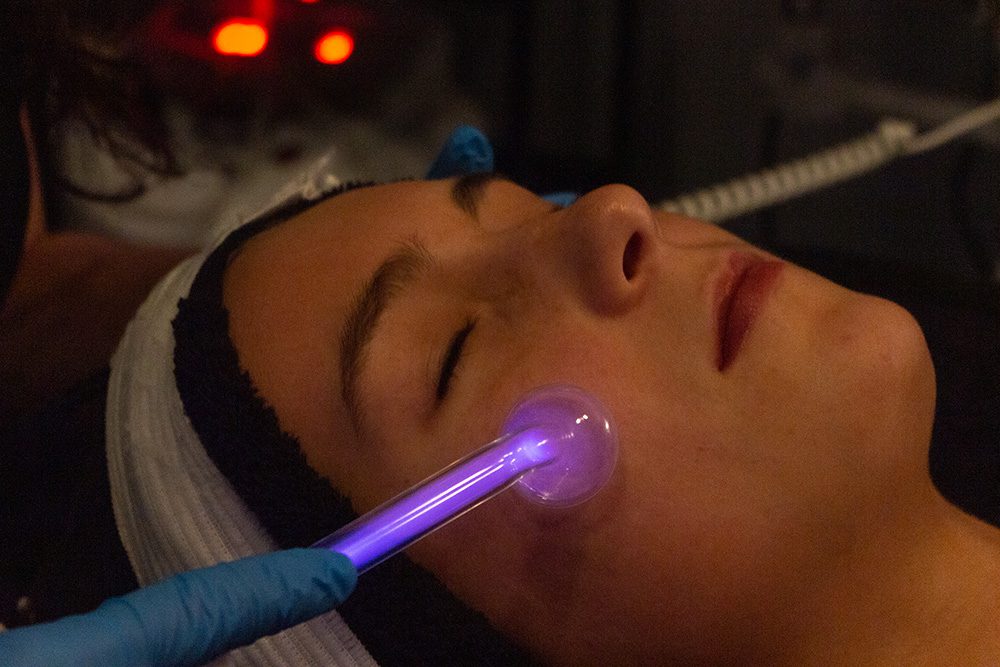 A woman getting a facial treatment with a purple light.