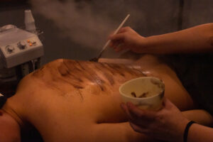 A woman is getting a body treatment with a cup of coffee.
